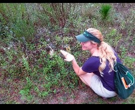 Heather crouching in brush, examining something in nature